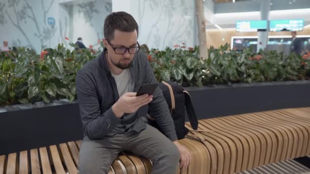 Viajero masculino está comprobando el correo electrónico por teléfono inteligente en el aeropuerto — Vídeos de Stock