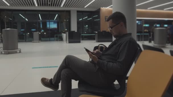 Pasajero masculino está esperando el embarque en el aeropuerto, utilizando el teléfono celular — Vídeo de stock