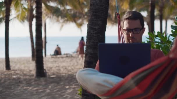 Интернет на берегу океана, человек отдыхает в гамаке — стоковое видео