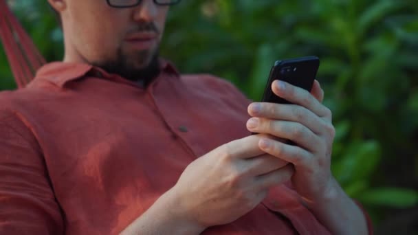 Мужчина сидит за смартфоном в саду — стоковое видео