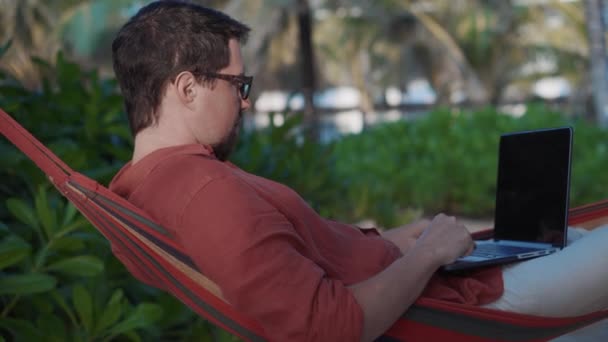 Freelancer werkt op afstand door notebook, liggend in hangmat — Stockvideo