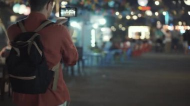 Adam gecenin bir yarısı şehrin caddesinde yürüyor ve akıllı telefonuyla film çekiyor.