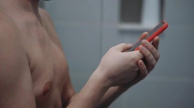 Banyoda cep telefonu olan bir adam, mesaj yazıyor ve daktilo ediyor.