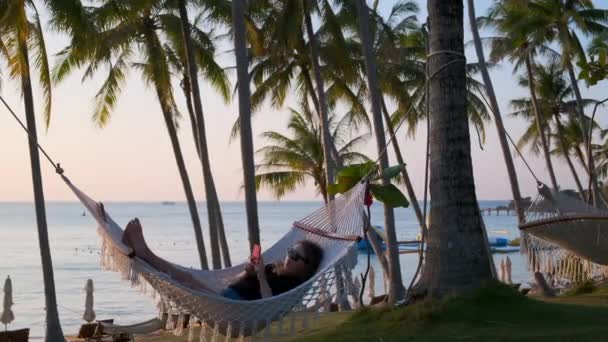 Jeune femme en vacances. Elle se relaxe dans un hamac au bord de la mer — Video