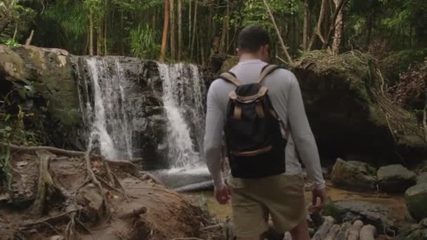 Turisti mies kävelee metsässä Aasiassa, katselu vesiputouksia — kuvapankkivideo