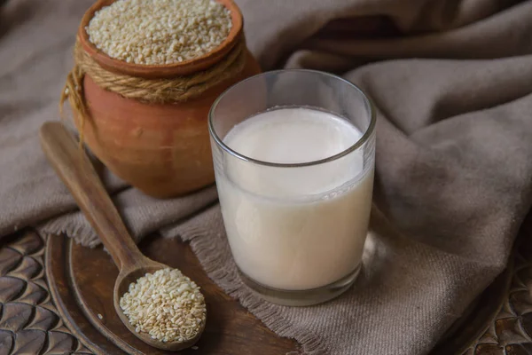 Кунжутное молоко в стакане и кунжутное семя в глиняном горшке на столе . — стоковое фото