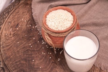 Ahşap bir masa üzerinde toprak kap içinde cam ve susam tohumu sütte susam.