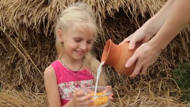 Menina bonita come flocos de milho com leite de um frasco de vidro em uma aldeia . — Vídeo de Stock