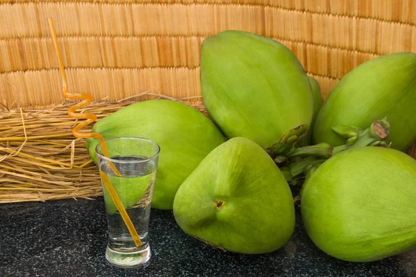 Verse groene kokosnoten tak en kokosnoot sap in een glas op zwart graniet. — Stockfoto