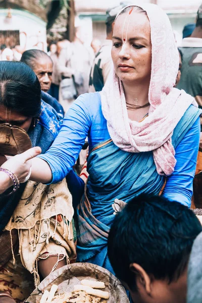 Agradwip, West-Bengalen, India - 8 dec 2019. mooie blanke vrouw in een hoofddoek dupata en blauwe sari distribueert heilig voedsel aan de Indiase bevolking. gratis voedselverstrekking in India. — Stockfoto