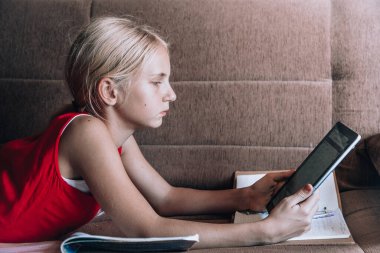 Koronavirüs. Evde kal. Kendini soyutlama konsepti. Sosyal uzaklık, Çevrimiçi eğitim serbest çalışma. Coronavirüs salgını dünyası. Koltuğunda, defterleri ve tabletleri olan güzel bir sarışın.