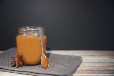 Ahşap masa üzerinde bir kavanoza tuzlu karamel sos. Siyah arka plan
