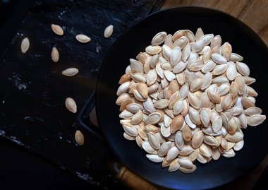 Kavrulmuş kabak çekirdekleri siyah bir tabakta koyu bir arka planda.