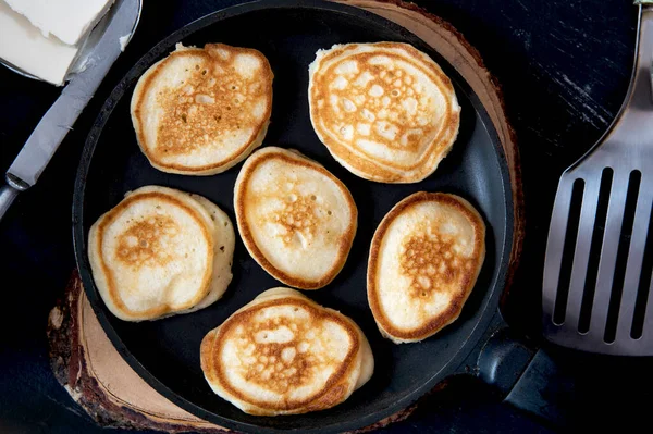 Small pancakes in a pan on a wooden board.