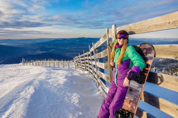 Jovem de sucesso snowboard nas montanhas Sheregesh. Snowboarder descansando. Elegante snowboarder caucasiano. Snowboarder sorrindo para a câmera no topo da montanha em um fundo do céu. — Fotografia de Stock