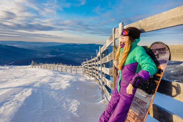 Erfolgreiche junge Snowboarderin in den Bergen sheregesh. Snowboarder rastet aus. stylischer kaukasischer Snowboarder. Snowboarder auf dem Gipfel des Berges vor blauem Himmel. — Stockfoto