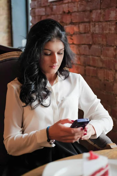 Una chica joven en el café hace negocios. Jovencita sosteniendo un smartphone. Trabajador de oficina en el almuerzo. reunión de negocios. enviar un mensaje . — Foto de Stock