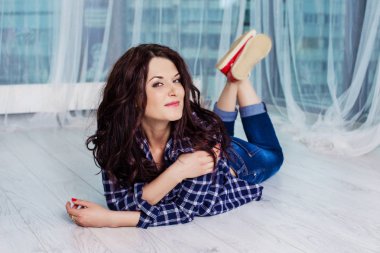 Hippi kız kameraya gülümseyen ve salıncakta oturuyor. Siyah kıvırcık saçlı mavi kareli gömlek, kot pantolon ve kırmızı spor ayakkabı giyen genç beyaz kız.