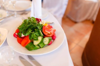Lezzetli yaz salatası beyaz tabakta taze sebze ile masaya servis. Salatalık, domates, turp ve marul.