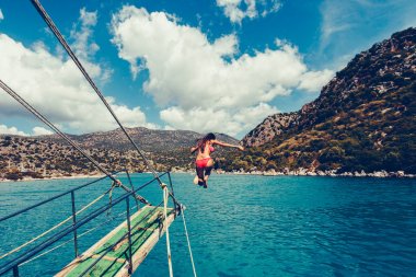 Kız dalışlar veya bir uzun atlama ile tekne bir peyzaj dağlar ile açık denize atlar. Vintage tonlu görüntü. Şık tonda resim.
