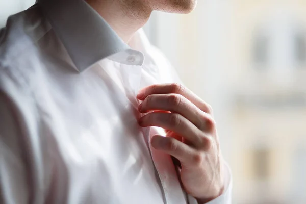 Man buttons up his white shirt standing in the front of a bright window — Stock Photo, Image