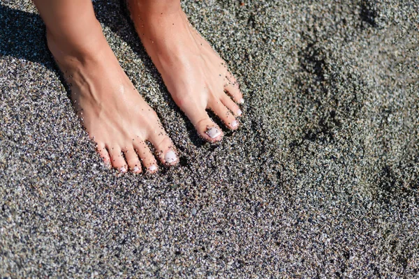 Pies de mujer con pedicura oscura relajándose en la arena —  Fotos de Stock