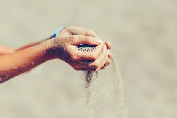 Sand Handvoll in weiblichen Händen an einem Strand gegen das Meer, durchtrainiert. Fallender Sand aus den Händen. — Stockfoto