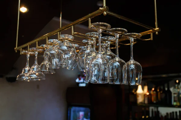 Glasses hanging over a bar rack,Cocktail glasses hanging over a bar,different glasses hanging over the bar. Soft focus,Clean washed and polished glasses,A pub.Bar.Restaurant.