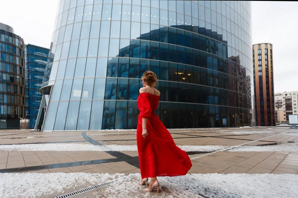 Joven hermosa chica rubia glamorosa en un vestido rojo posando cerca de escaparate de cristal en el centro de negocios. Foto amplia . —  Fotos de Stock