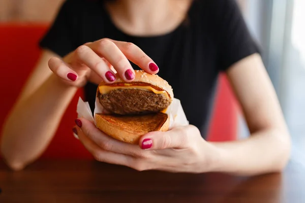 Menina segurando em mãos femininas hambúrguer fast food e mostra o que ele é feito de, refeição calorias americanas pouco saudáveis em segundo plano, com espaço de cópia para mensagem de texto ou design, humano com fome com grelhados — Fotografia de Stock