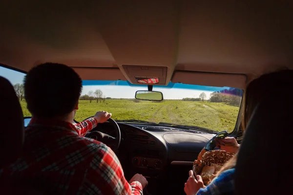 Una giovane coppia si reca in camicie e pantaloncini, seduta in macchina. I turisti vanno sulla jeep accanto all'erba fissando l'orizzonte. Con spazio per il tuo testo. Viaggio e avventura concetto . — Foto Stock