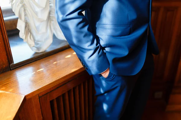 Pria dengan setelan biru mengkilap memegang tangannya di saku, bersandar pada sill closeup kayu dari tangan pengusaha di saku — Stok Foto