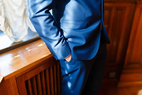 El hombre con el traje azul brillante sostiene sus manos en sus bolsillos, apoyándose en un alféizar de madera cerca de manos de hombre de negocios en bolsillos — Foto de Stock