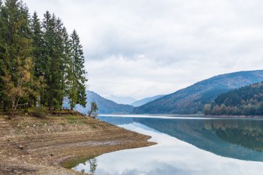 Ağaçları ve güzel bulutlu gökyüzü sonbaharda yansıtan ile dağ gölü