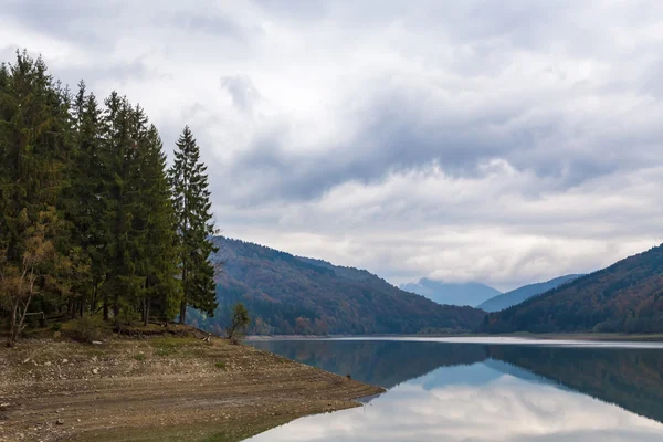 Ağaçları ve güzel bulutlu gökyüzü sonbaharda yansıtan ile dağ gölü