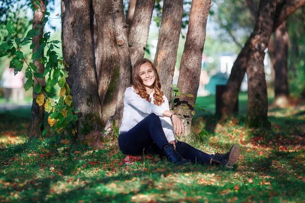 Young beautiful woman. Beauty teenager girl sitting in autumn park — Stockfoto