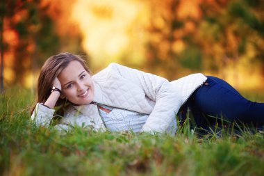 Young woman, beautiful girl lying on grass in autumn park