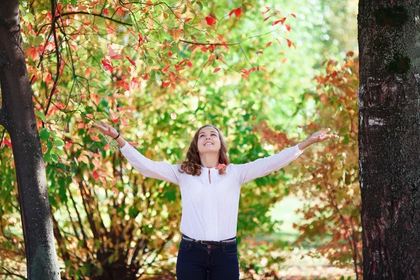 Young beautiful teenager girl tosses colorful autumn leaves in park