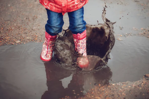 Kind in rosa Regenstiefeln springt in eine Pfütze — Stockfoto