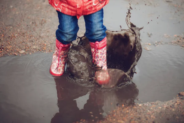 Niño con botas de lluvia rosa saltando en un charco — Foto de Stock