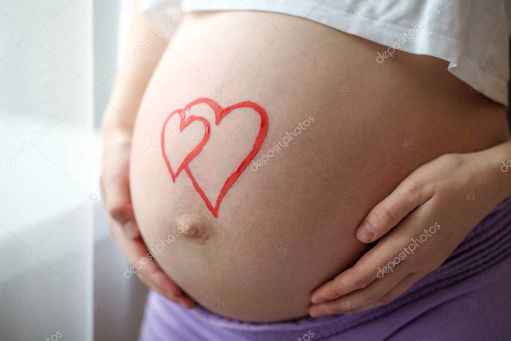 Young pregnant woman holding and touching her belly, closeup