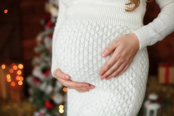 Έγκυος γυναίκα κρατώντας μια κοιλιά κοντά στο χριστουγεννιάτικο δέντρο — Φωτογραφία Αρχείου