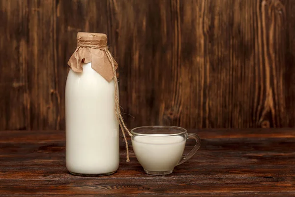 Fles melk en cup op rustieke houten tafel — Stockfoto