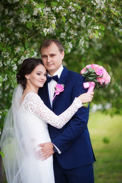 Jovem noivo e noiva com buquê de casamento no jardim florescente — Fotografia de Stock