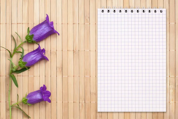 Caderno em branco em um fundo de bambu e flor de sino, espaço de cópia — Fotografia de Stock