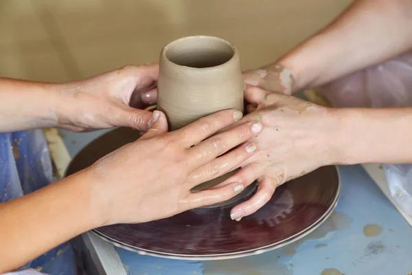 As mãos de duas pessoas criam o pote, a roda de oleiro. Ensino de cerâmica — Fotografia de Stock