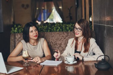 Dizüstü bilgisayar ile beyaz iş kadınları gülümseyen iki genç. Kadınlar Cafe