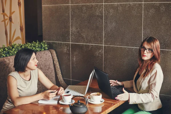 Duas jovens empresárias caucasianas com portátil, caderno. Mulheres no café — Fotografia de Stock