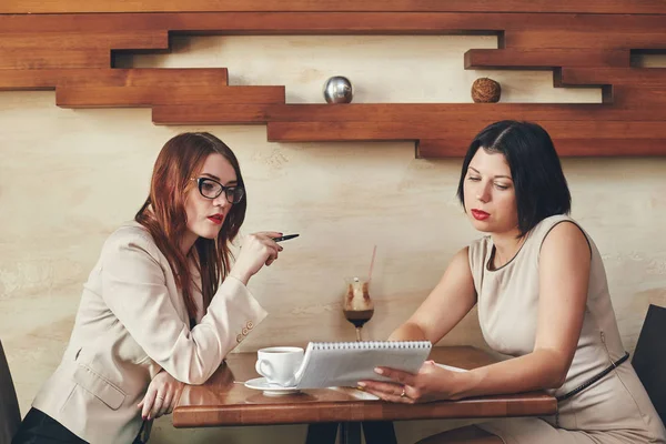 İki genç beyaz iş kadınları defter ile. Kadınlar Cafe
