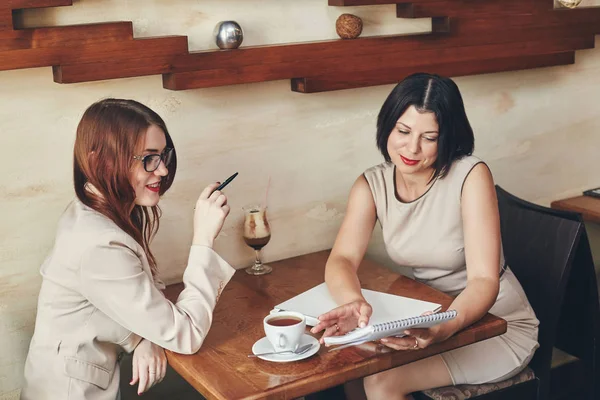 Dos jóvenes mujeres de negocios caucásicas sonrientes con cuaderno. Mujeres en la cafetería — Foto de Stock
